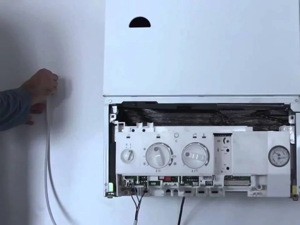 Professional technician in a white hard hat installing a digital thermostat on a white interior wall in San Antonio.